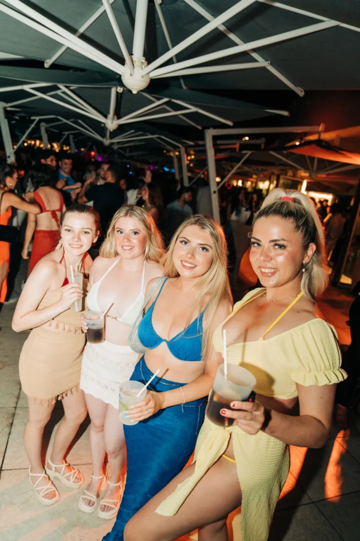 Girls raising cocktails under umbrellas at Cafe Del Mar Malta, glowing skin, loud tunes and a packed dance floor all night