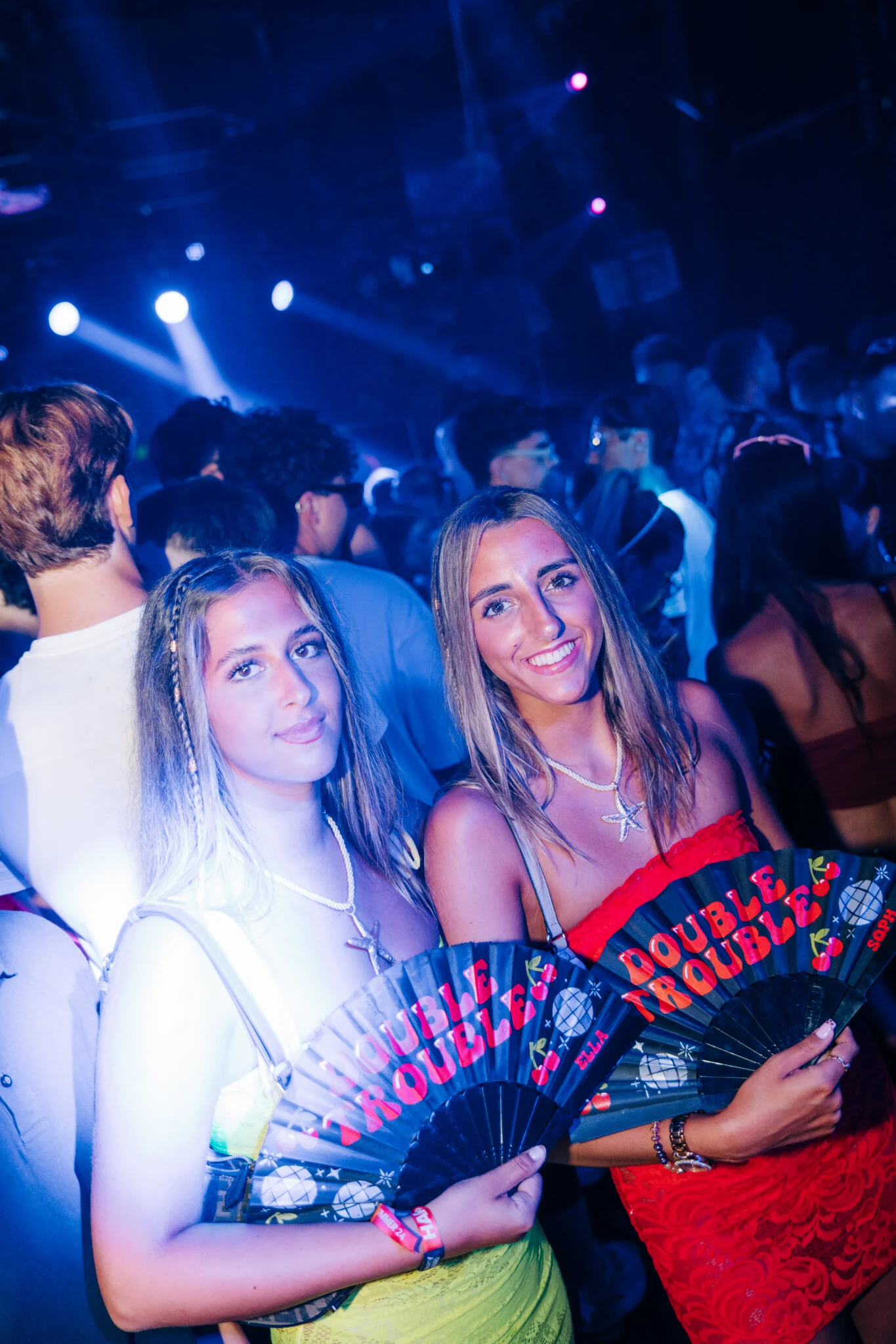 Two girls holding Double Trouble fans and smiling on the packed dancefloor at Toy Room Super Club Night in Malta