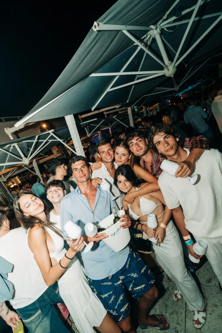 Big group raising glasses at Cafe Del Mar Malta, white outfits glowing under night lights and DJs keeping the terrace jumping