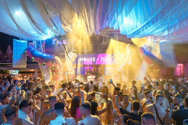Packed dancefloor facing the DJ booth at House in Paradise at O Beach Ibiza with glowing lights, hanging fabric and giant tentacles