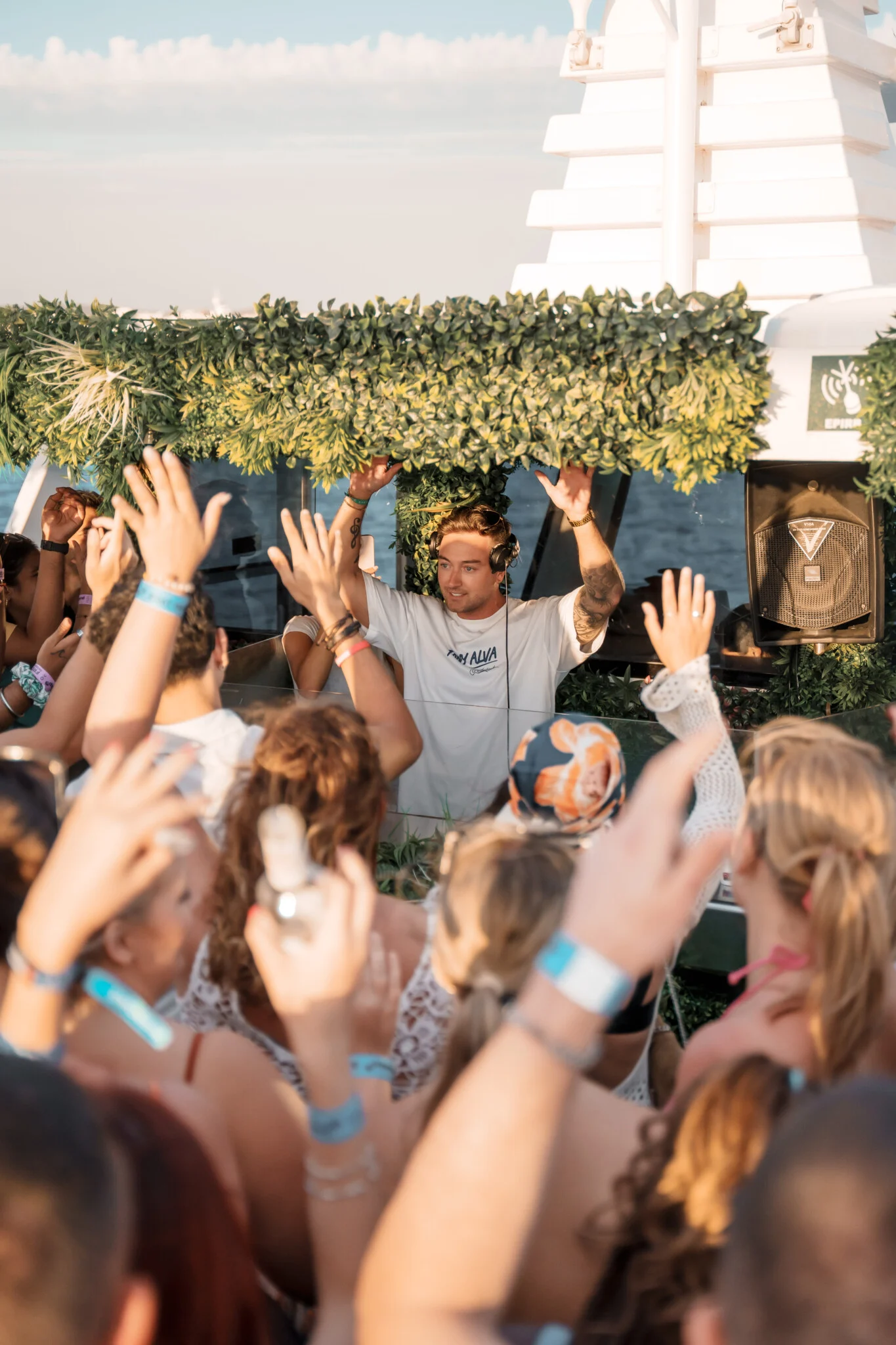 DJ with both hands raised behind the booth as the crowd reaches up on a Pukka Up boat party in Ibiza