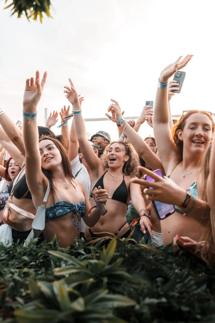 Girls at the front of the crowd with arms raised and phones out on an Ibiza Pukka Up booze cruise in daylight