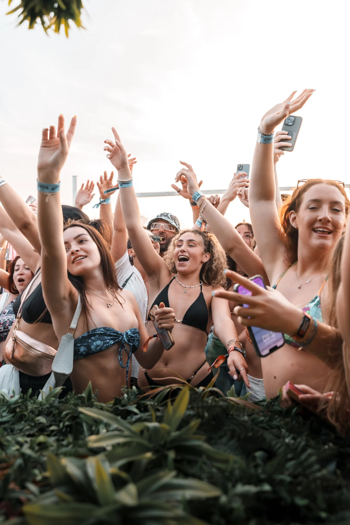Girls at the front of the crowd with arms raised and phones out on an Ibiza Pukka Up booze cruise in daylight