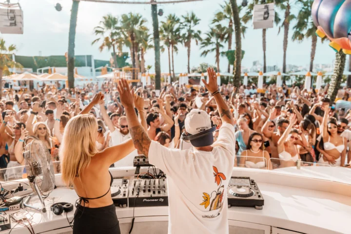 DJ's with both arms raised behind the booth as the House in Paradise crowd fills O Beach Ibiza