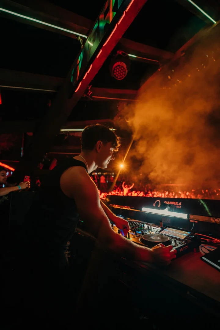 DJ performing at Gianpula Club Night in Malta, mixing on stage with smoke effects and a packed crowd lit up in the background.