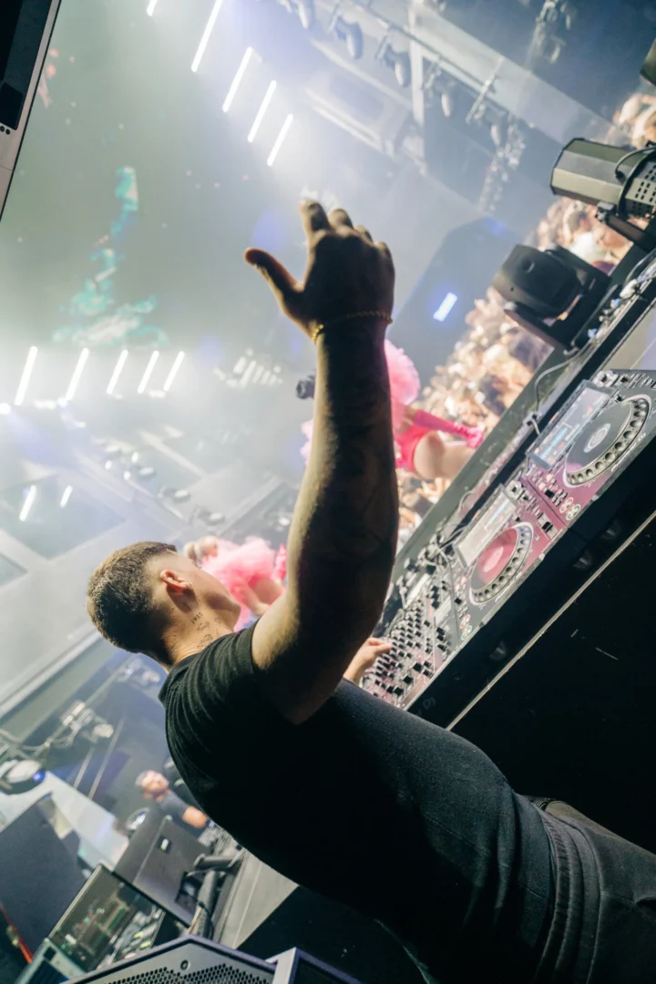 DJ raising his arm behind the decks during Toy Room Super Club in Malta with the crowd and dancers in the background