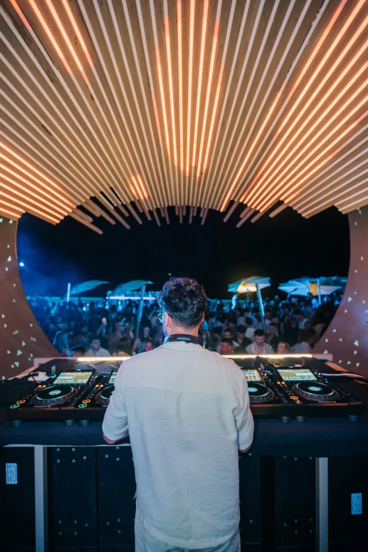 DJ dropping sunset beats at Cafe Del Mar Malta, packed terrace bouncing under glowing light canopy and open air dancefloor vibes