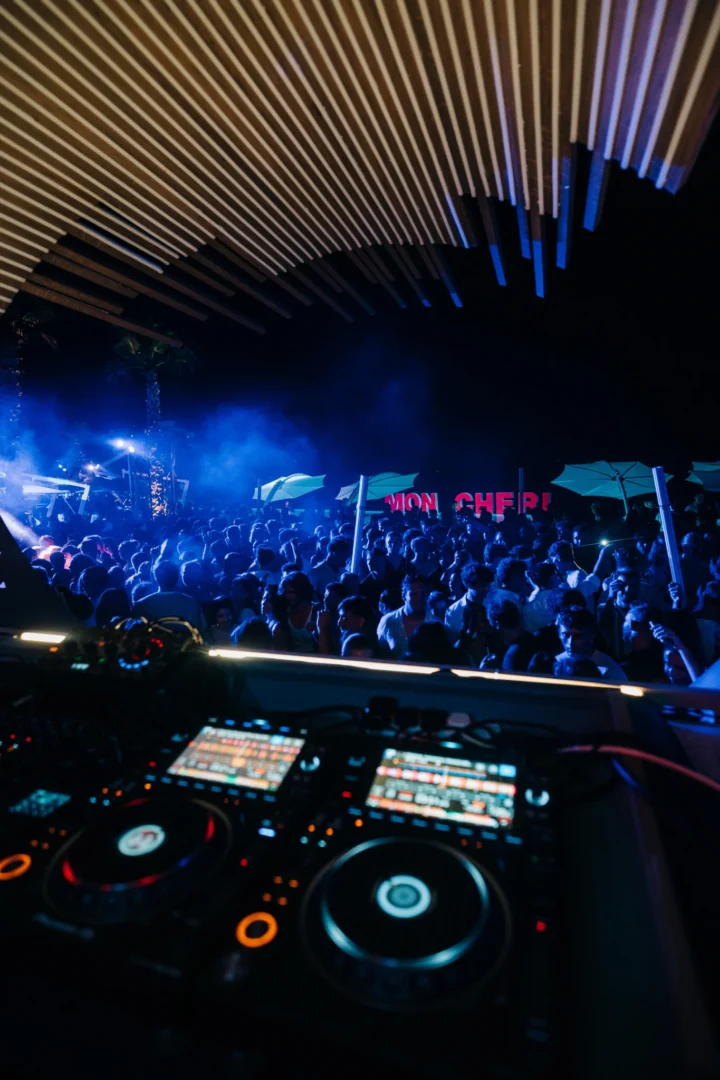 Blue-lit crowd surging at Cafe Del Mar Malta as DJs run the decks under the curved light canopy and the terrace turns into a full dance zone