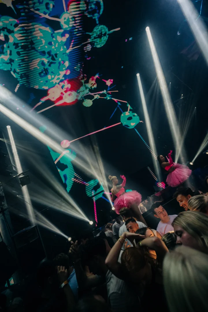 Stage dancers in pink outfits above the crowd at Toy Room Super Club with bright light beams and LED visuals