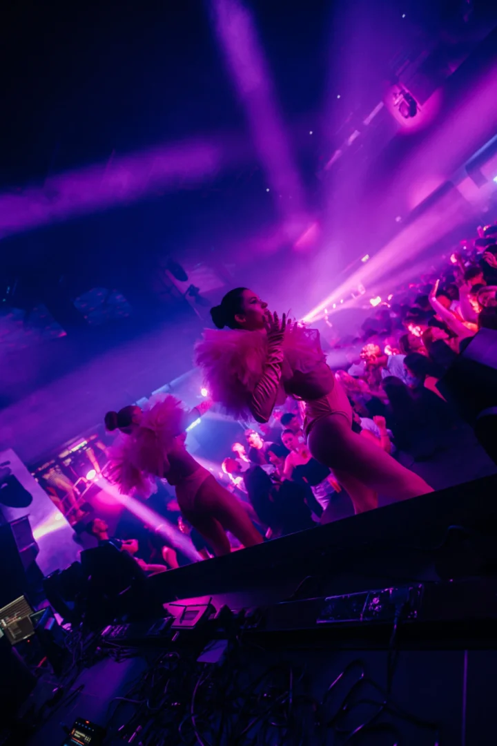 Two stage dancers performing above the crowd under purple lighting at Toy Room Super Club in Malta