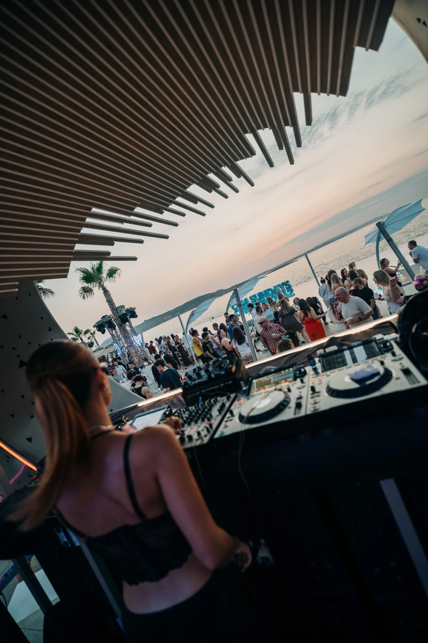 DJ lining up sunset tunes at Cafe Del Mar Malta as the crowd fills the terrace and the sea glows behind the decks