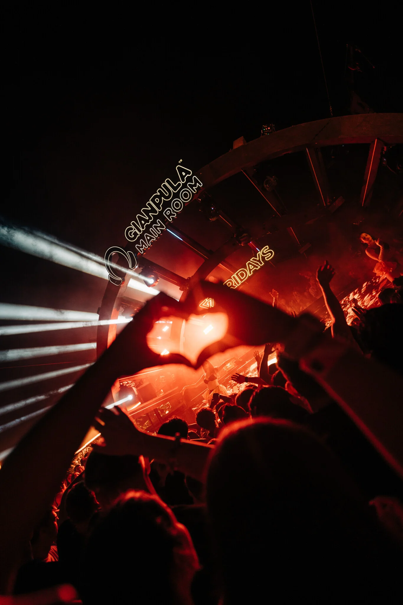 Crowd at Gianpula Fridays Club Night in Malta making a heart shape with hands as red lights and stage beams hit the dancefloor.