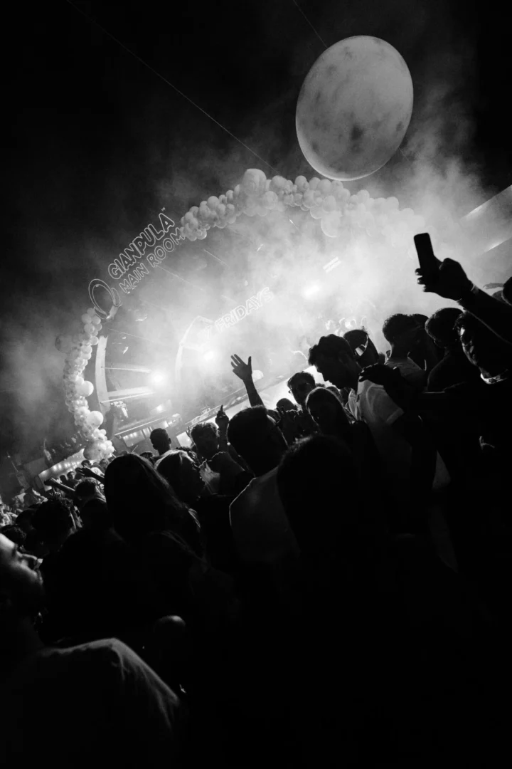 Black and white crowd scene at Gianpula Club Night in Malta with smoke, raised phones and silhouettes facing the lit-up stage.