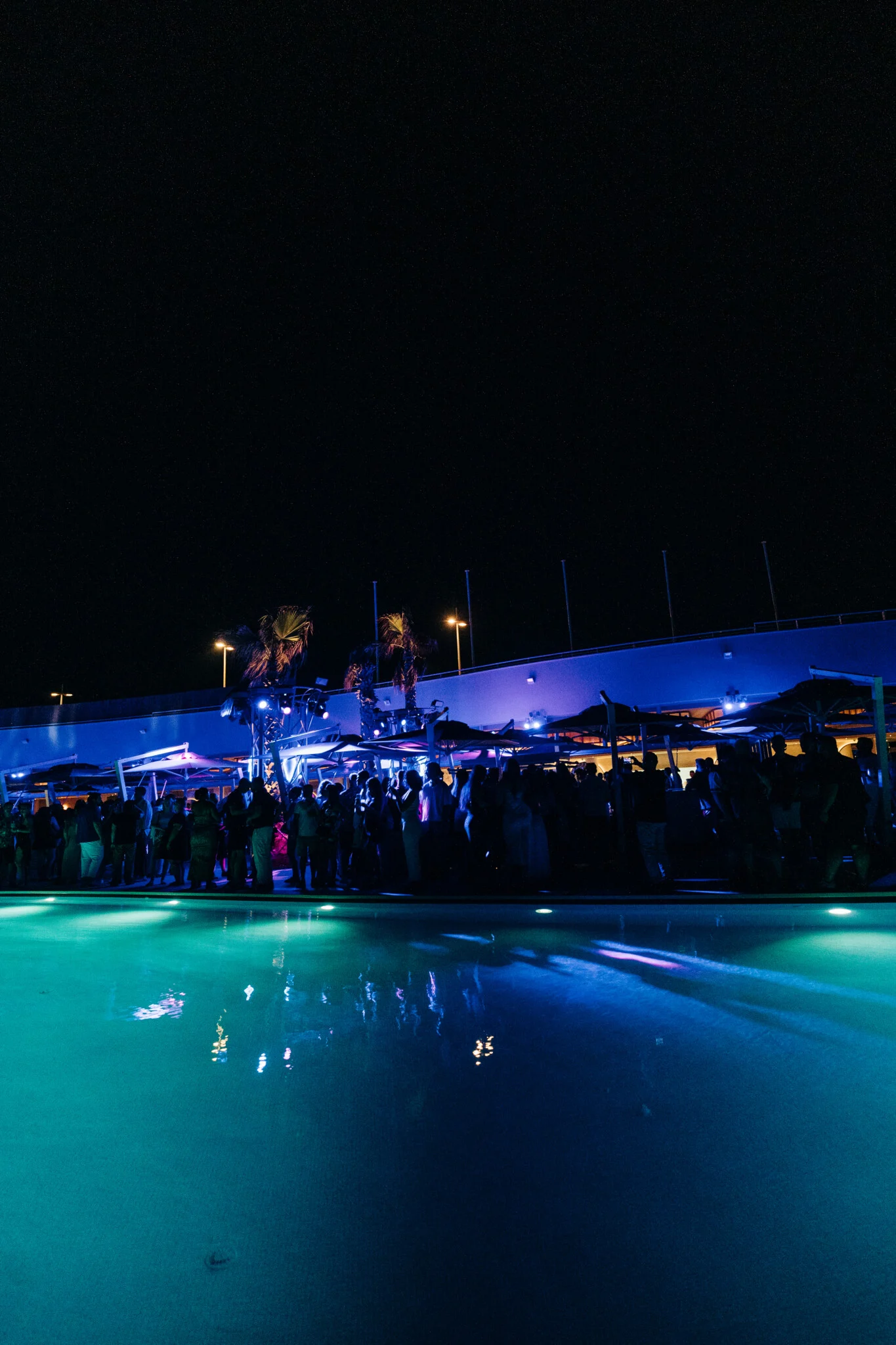 Late night poolside session at Cafe Del Mar Malta glowing in neon blue as the terrace fills with party crowds and open bar vibes