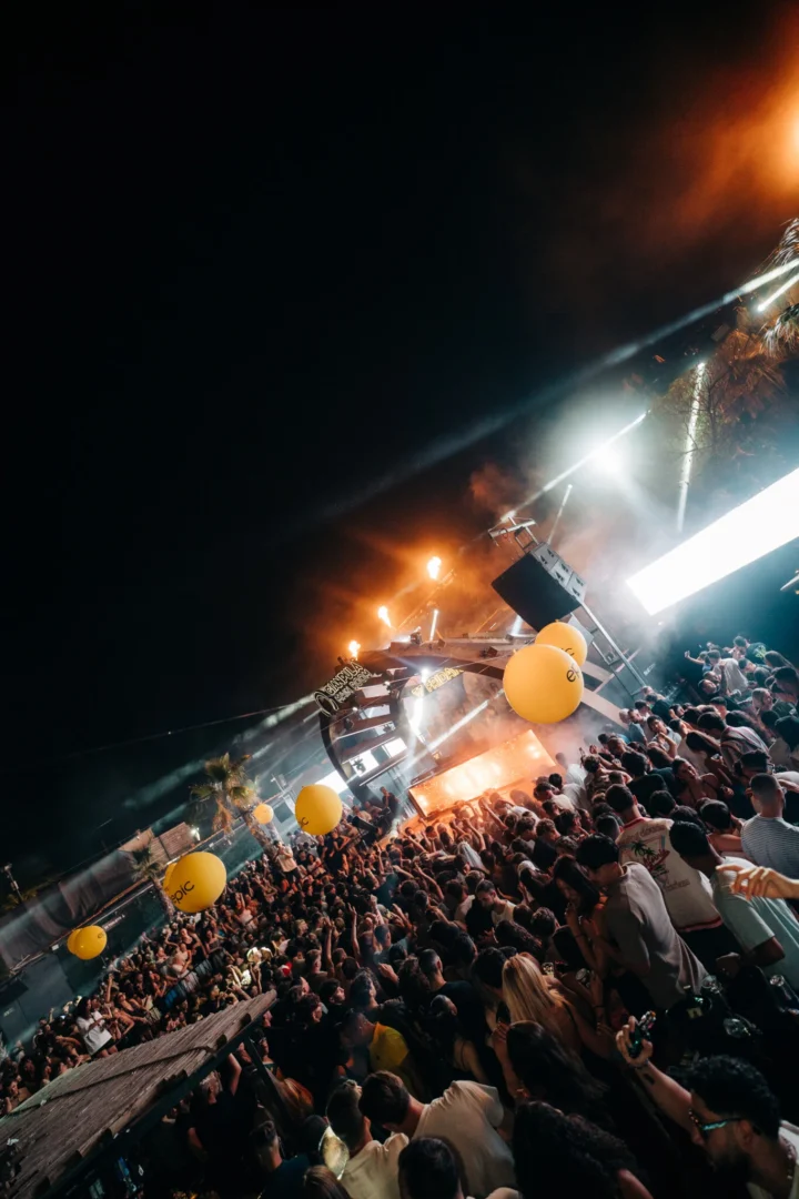 Wide view of Gianpula Club Night in Malta with a huge crowd, bright stage lights, smoke and yellow balloons above the dancefloor.