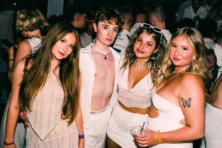 Friends dressed in white posing together at Agenda White Party, drinks in hand and dancefloor energy all around