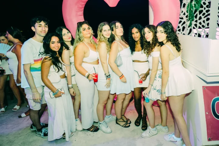 Group of friends in all-white outfits posing with drinks at the Agenda White Party, soaking up the electric nightlife atmosphere