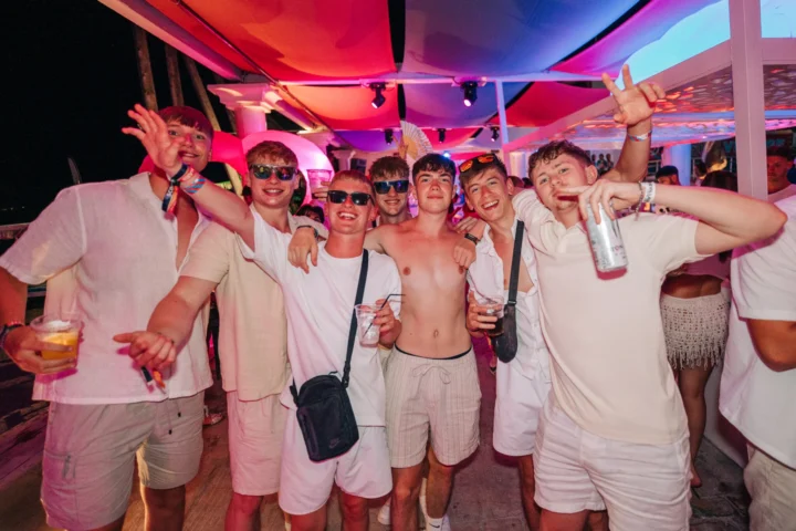 Group of mates going all in at Agenda White Party, drinks up and arms round shoulders as the night kicks into gear