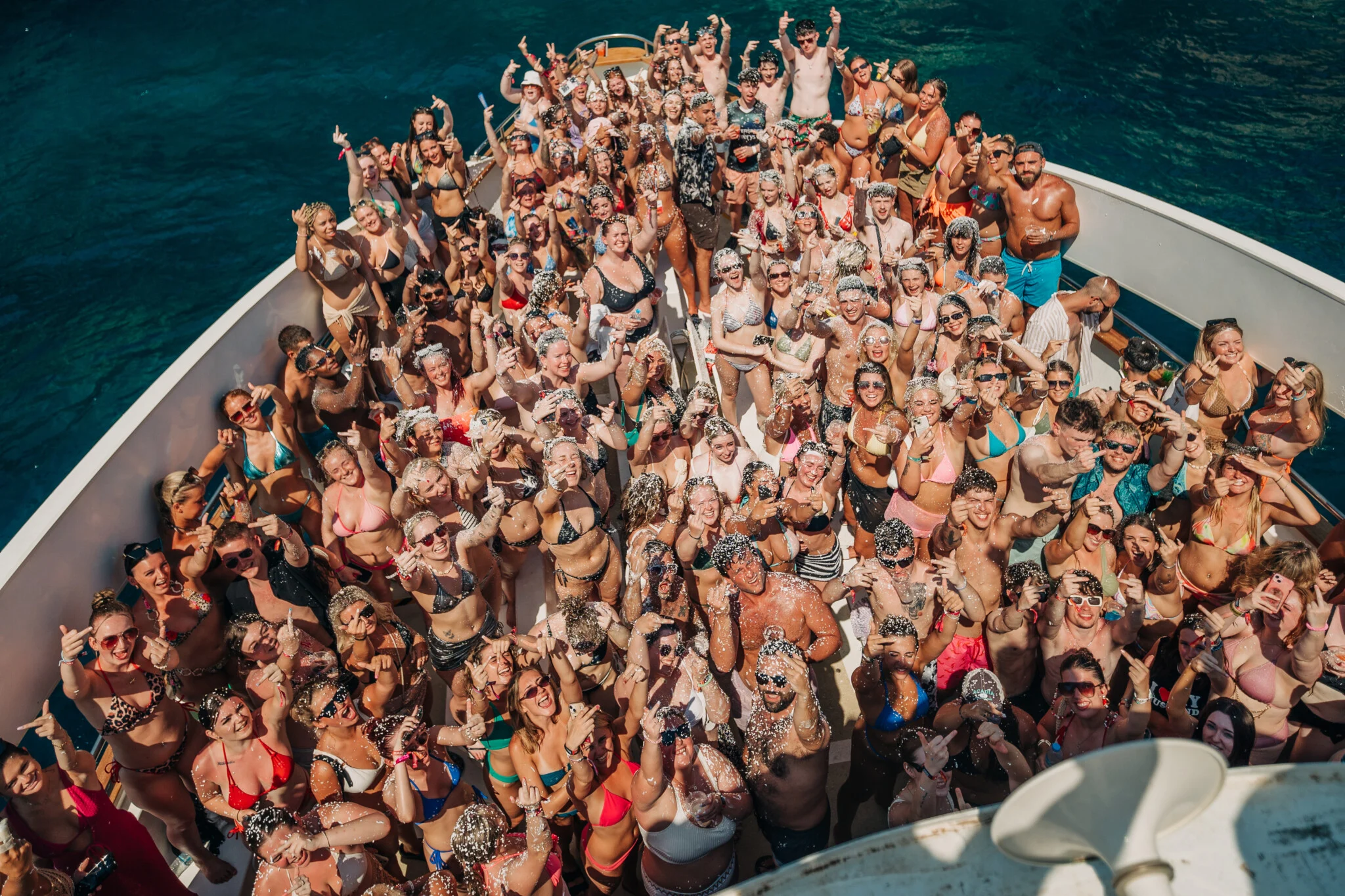 Overhead view of a packed Kavos boat party booze cruise with the crowd posing, cheering and covered in foam on the deck