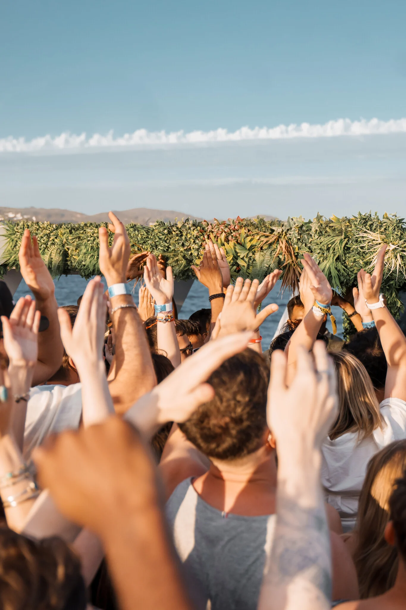 Crowd with hands raised above the deck on an Ibiza Pukka Up booze cruise with sea and hills in the background