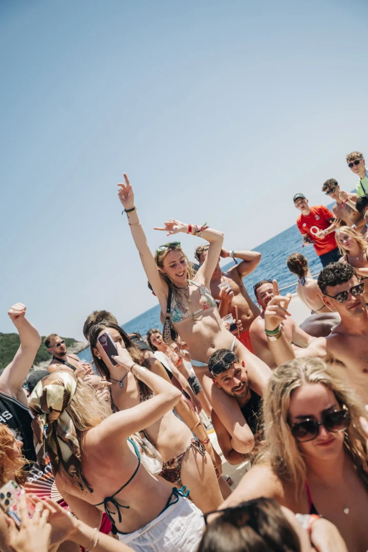 Girl rides on a lad’s shoulders as lads and girls dance on the Kavos Booze Cruise, drinks up and hands in the air