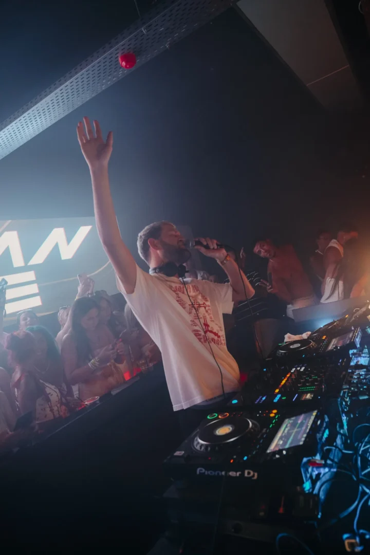 Nathan Dawe hypes the crowd at Agenda White Party in Kavos, mic up, hand raised as the room explodes around the DJ booth