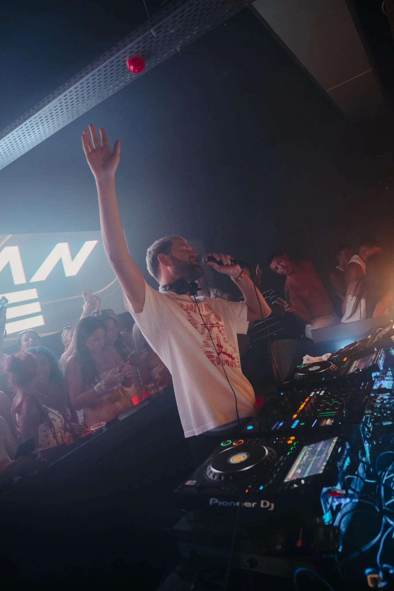 Nathan Dawe hypes the crowd at Agenda White Party in Kavos, mic up, hand raised as the room explodes around the DJ booth