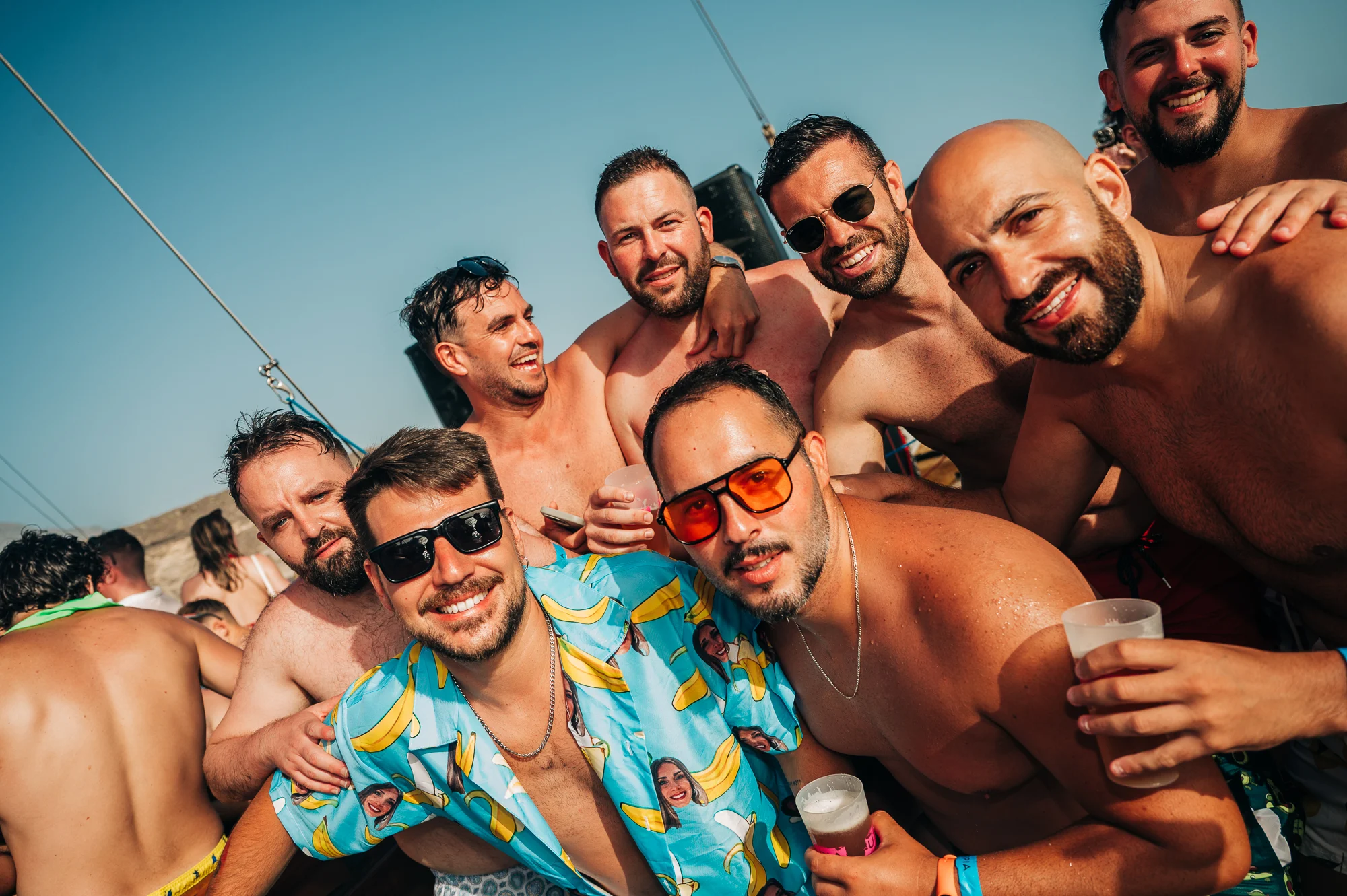 Lads packed together on a Tenerife boat party, beers in hand, sunshine out and full send daytime vibes on deck