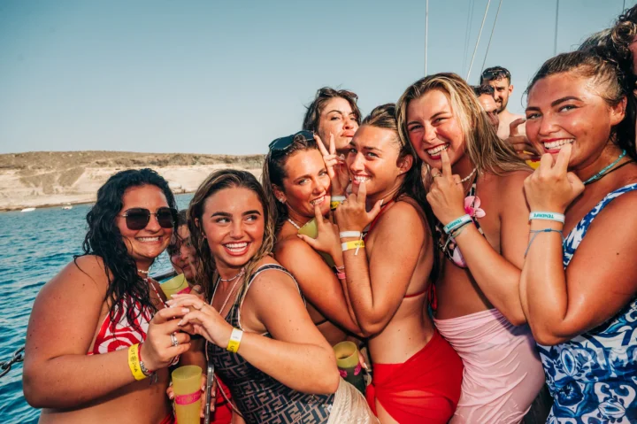 Girls posing on a Tenerife boat party, drinks in hand, laughing together with ocean views and big daytime energy