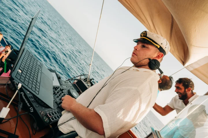 DJ mixing live on a Tenerife boat party, sea behind, decks loaded and daytime beats driving the crowd