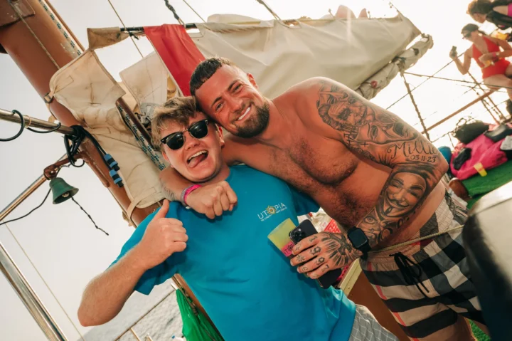 Two lads hugging on a Tenerife boat party, drinks in hand, sun blazing and proper daytime party vibes on deck