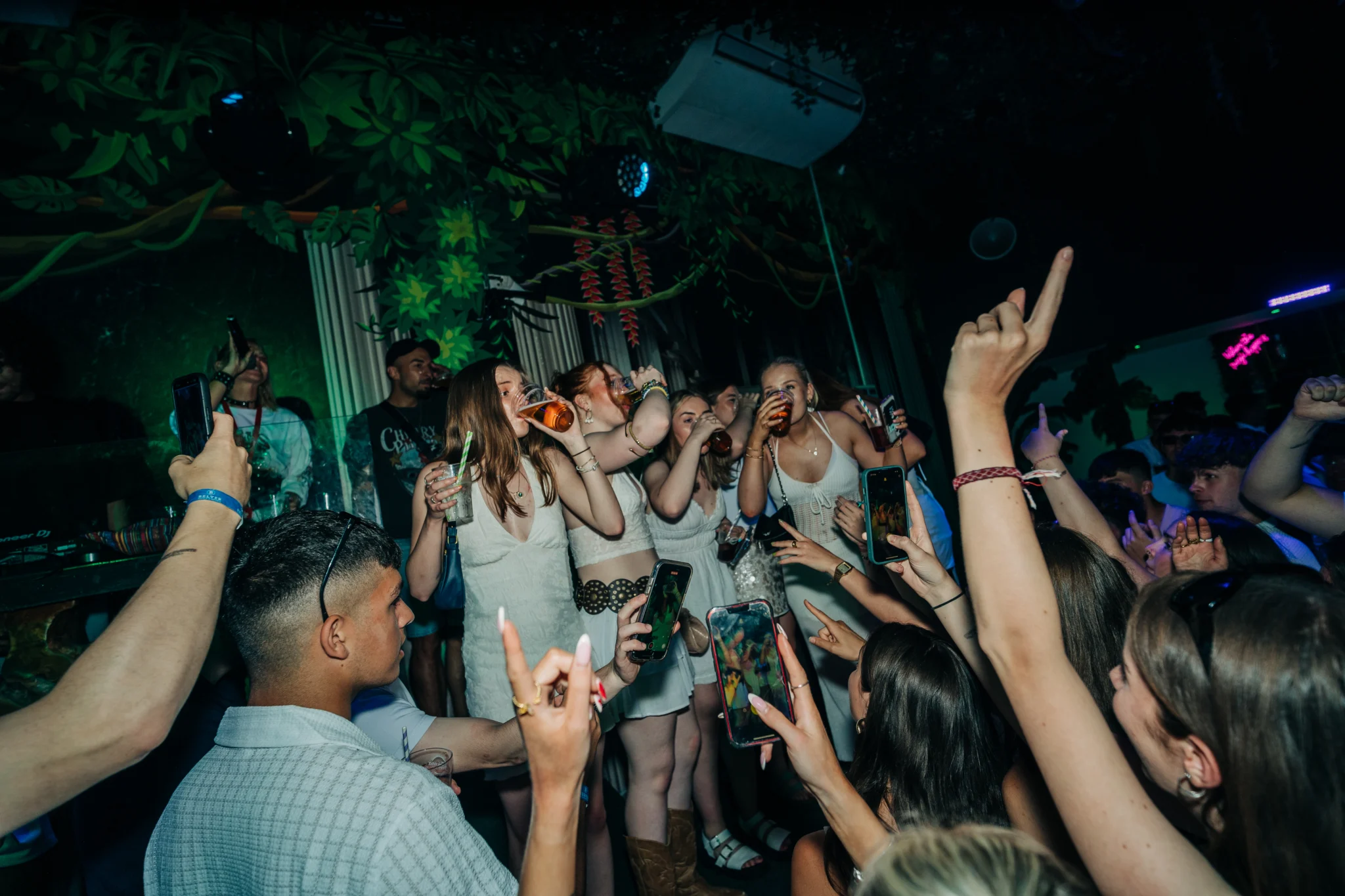 Party crowd cheering on the Albufeira Bar Crawl as a group of girls raise their drinks in the middle of the nightclub
