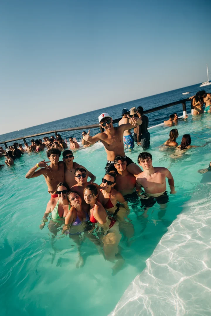 Group of girls and lads in the pool at the Toy Room Beach Club Party in Malta, posing together with sea views and a packed crowd behind them.