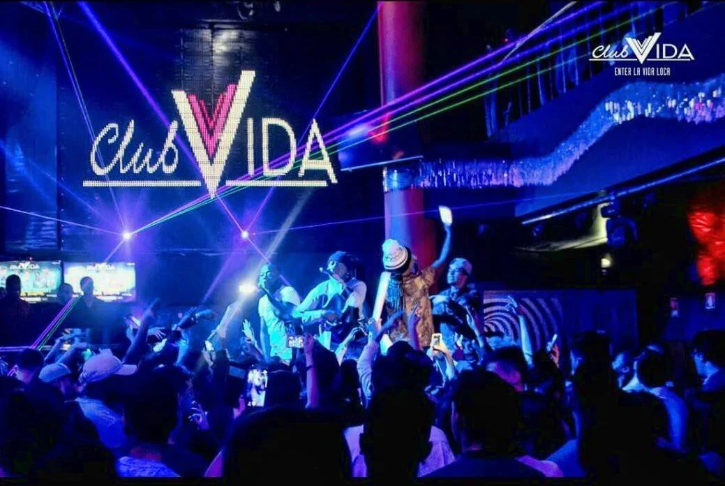 Lively scene at Club Vida in Albufeira, with performers on stage and a vibrant crowd under neon lights and laser effects.