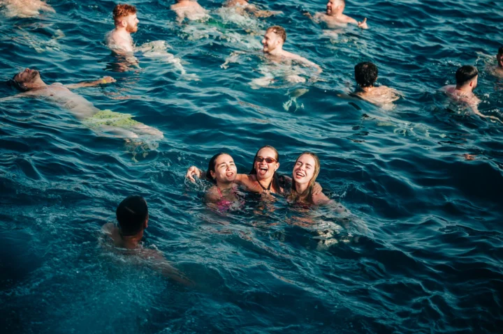 Girls laughing in the sea at a Tenerife boat party, lads swimming around them with sunshine and open-water vibes