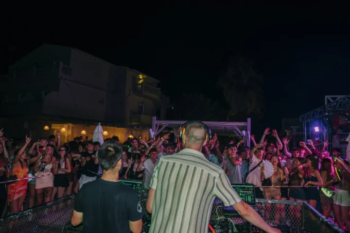 DJ drops heat in Kavos as the crowd goes wild, hands up, lights flashing and the night exploding in front of the decks
