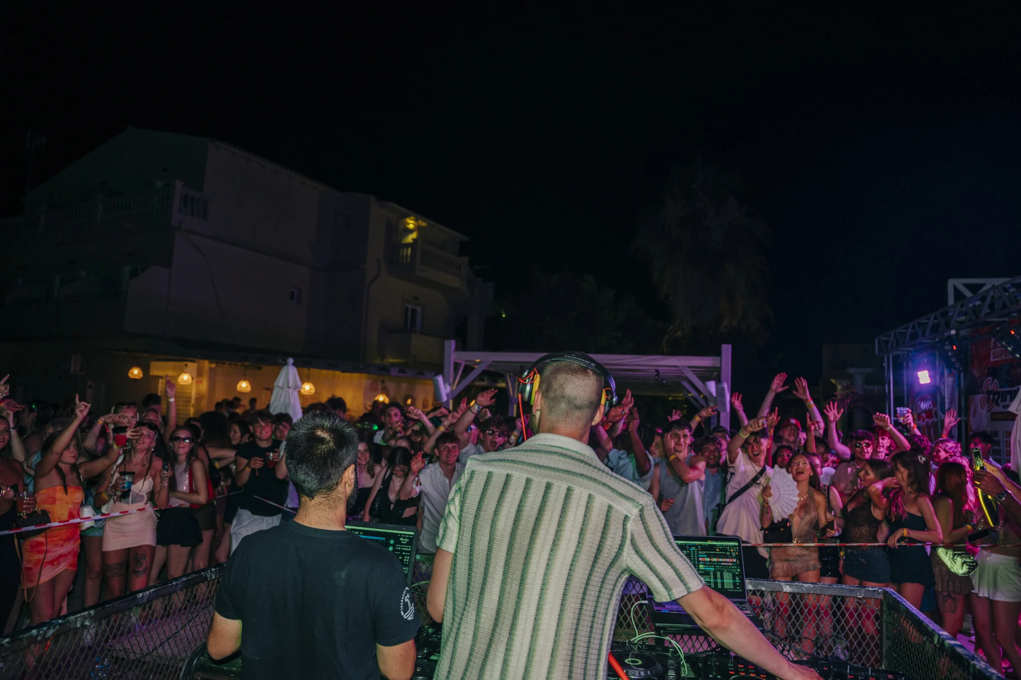 DJ drops heat in Kavos as the crowd goes wild, hands up, lights flashing and the night exploding in front of the decks