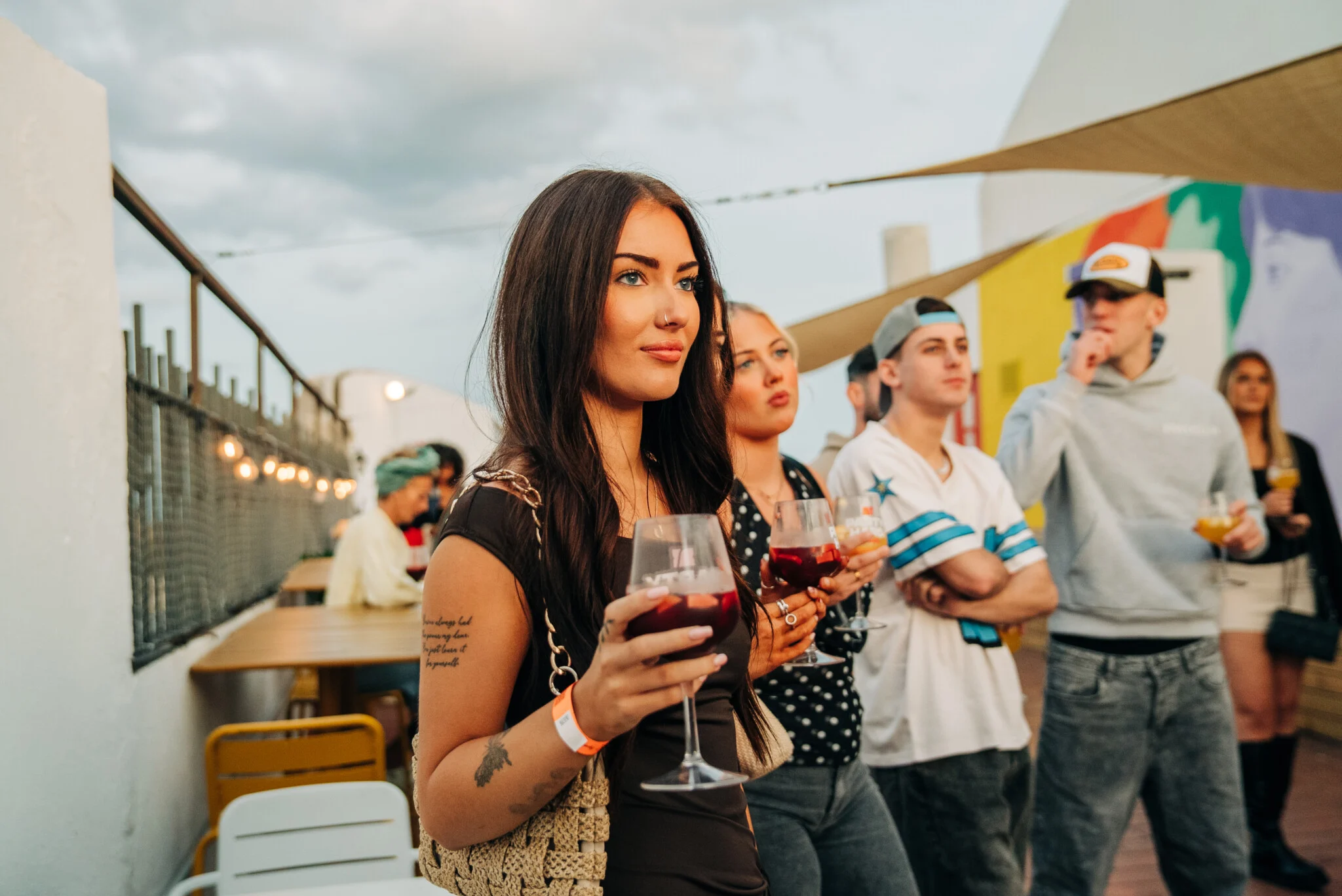 Girls and lads enjoying drinks at a Barcelona rooftop bar during the Barcelona Pub Crawl, with evening light and skyline views around them.