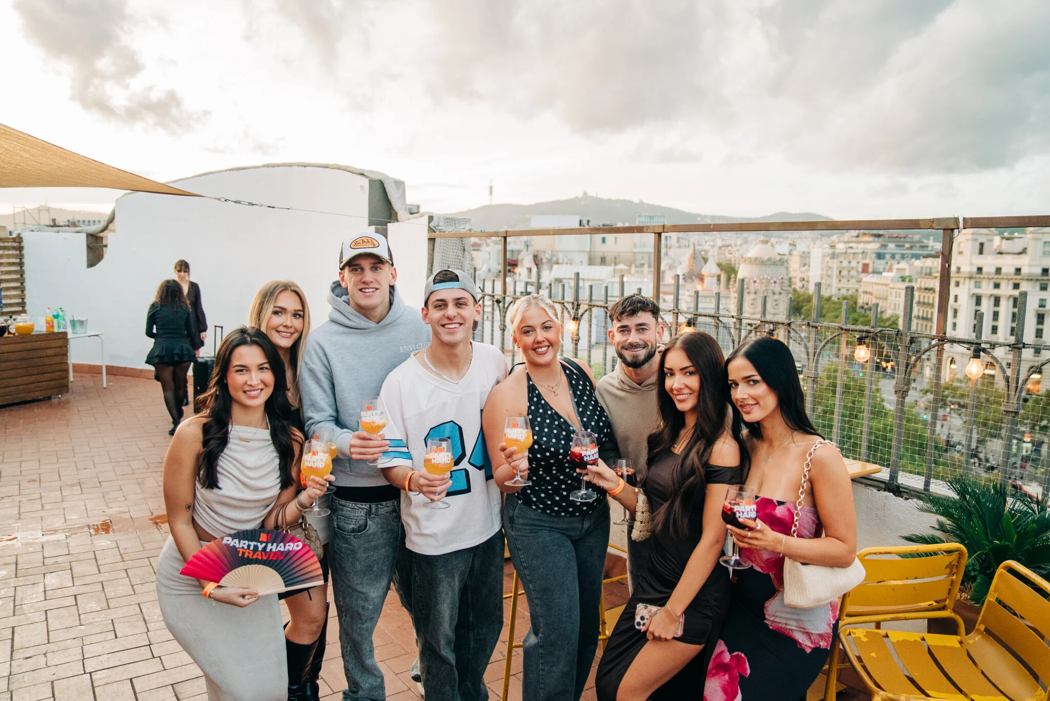 Group of girls and lads at a Barcelona rooftop bar during a Barcelona Pub Crawl, holding drinks with city views behind them.