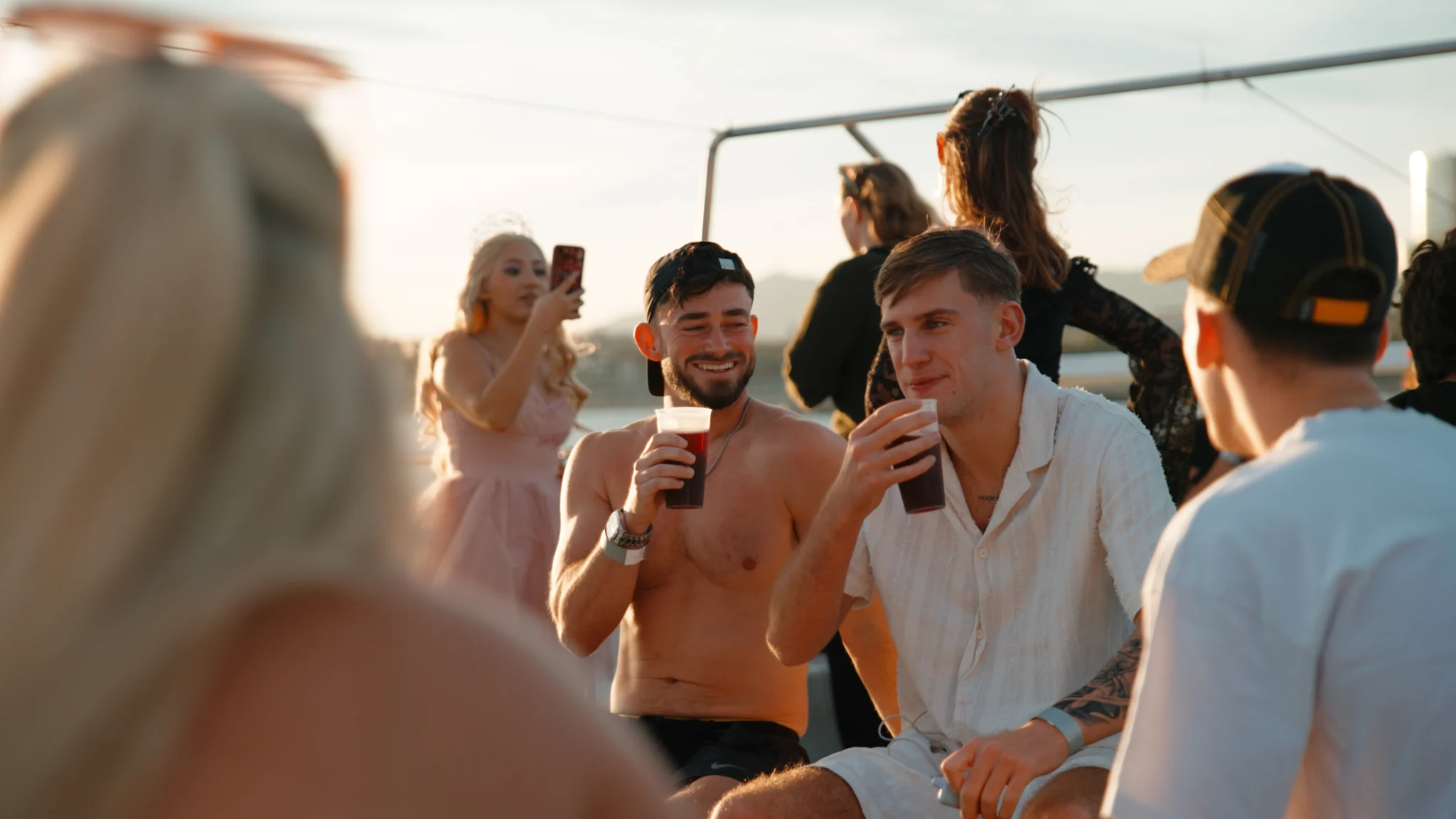 Lads relaxing with drinks on deck at the Barcelona Boat Party during sunset, with other guests enjoying the boat around them.