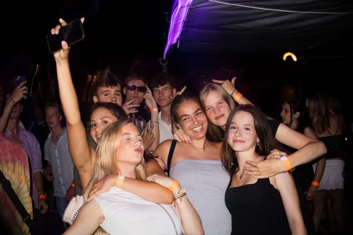 Group of girls and lads posing together at Split After Dark in Croatia, with one girl holding up a phone under purple club lights.