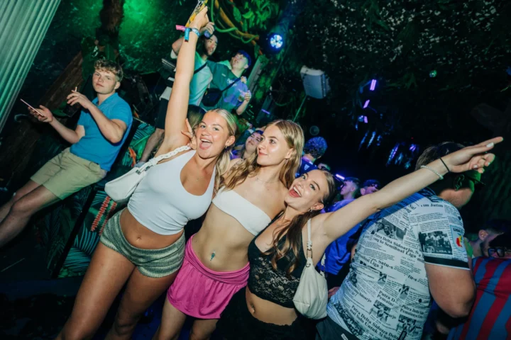 Three girls posing at Love Juice Residency Albufeira with arms in the air as the club crowd parties around them