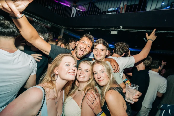 Group of girls and lads posing together at House of Tech Albufeira in a packed nightclub with drinks and hands in the air