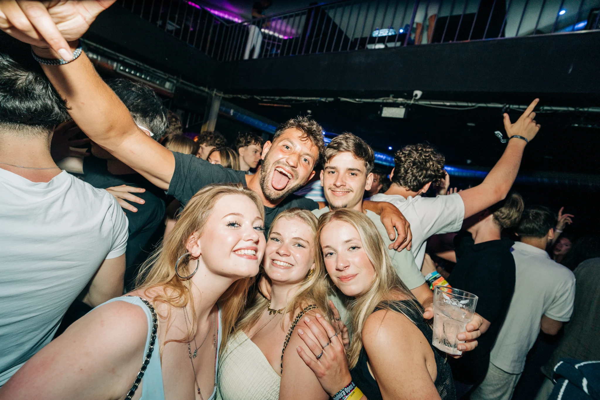 Group of girls and lads posing together at House of Tech Albufeira in a packed nightclub with drinks and hands in the air