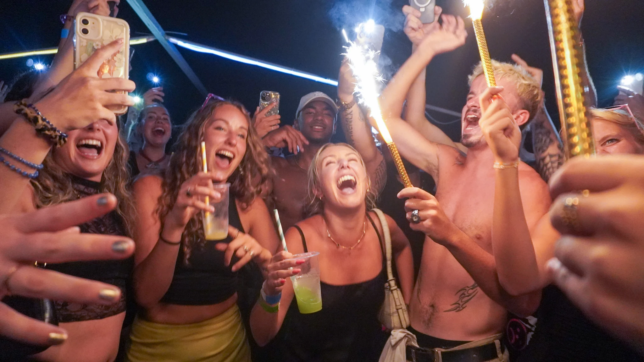 Crowd of girls and lads celebrating at Split After Dark in Croatia with sparklers, raised drinks and phones lighting up the dancefloor.