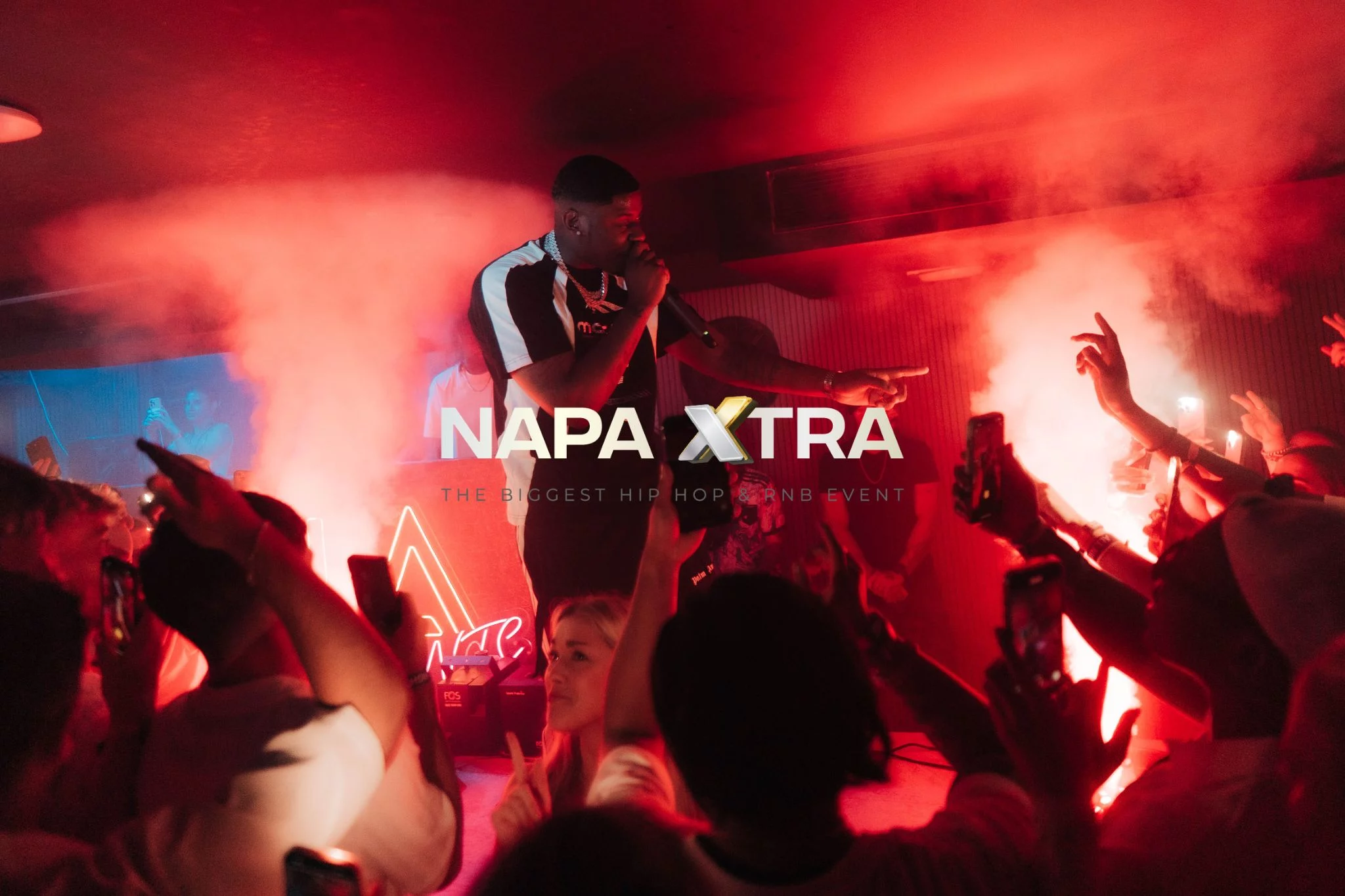 Live performer on stage with smoke jets and crowd holding up phones at Napa Xtra event in Aqua Club Ayia Napa