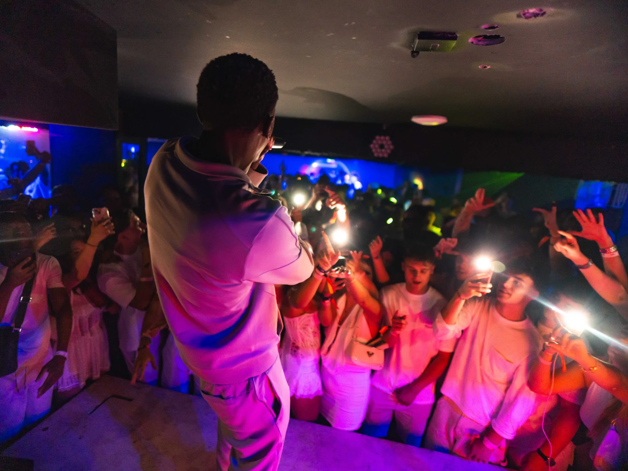 Rapper performing from the stage while the front row lights up the room with phones at Napa Xtra in Ayia Napa