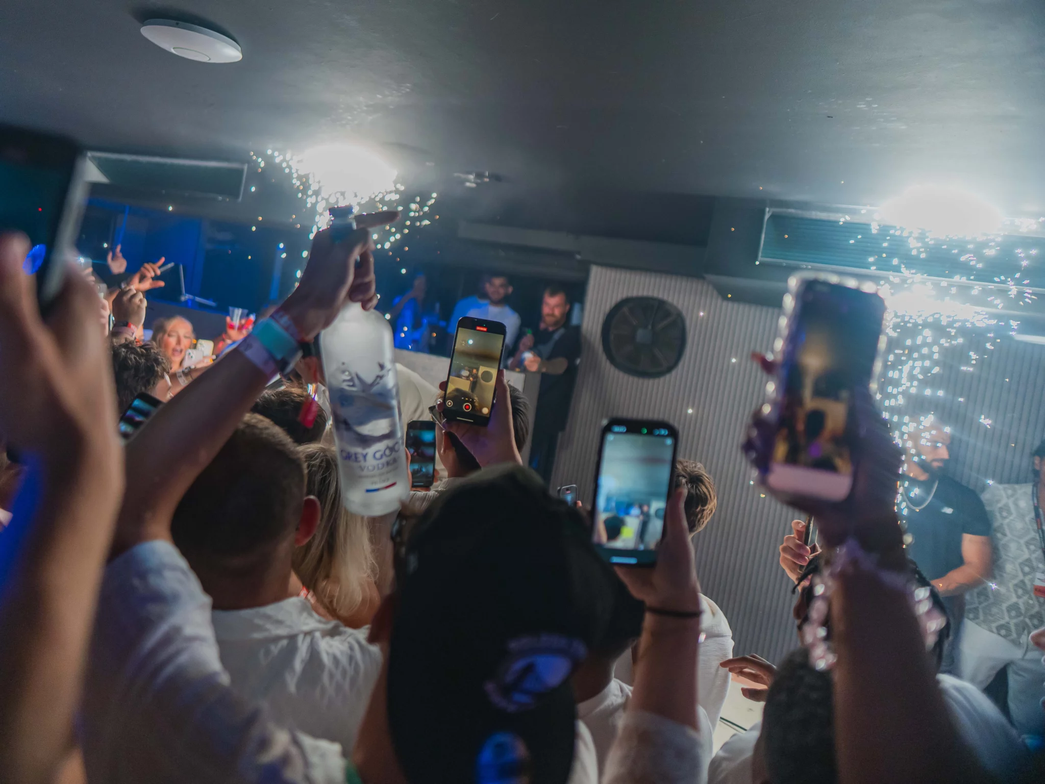 Crowd holding up phones and a Grey Goose bottle as sparklers light the room at Napa Xtra at Aqua Club