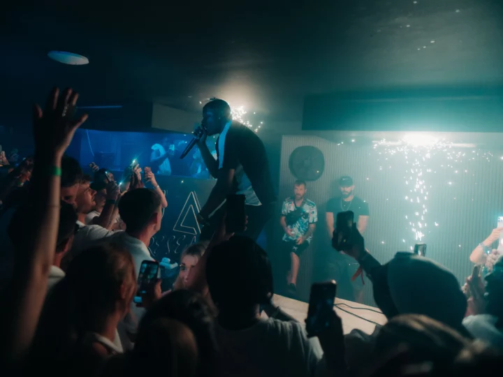 Napa Xtra artist on the mic above the front row at Aqua Club in Ayia Napa as phones glow and sparklers hit the room